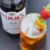 Pimms half and half with fruit skewers with a Pimms bottle next to the glass