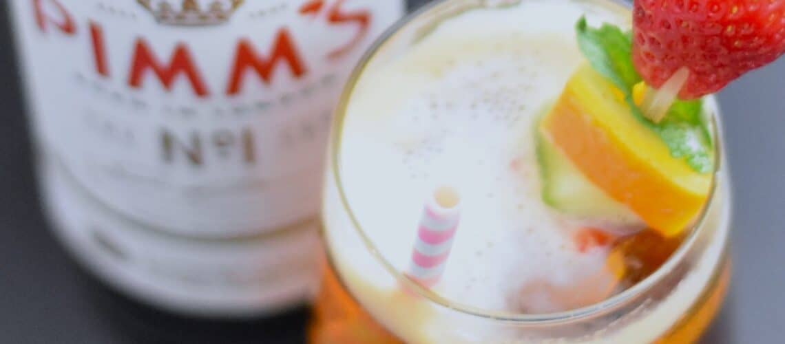 Pimms half and half with fruit skewers with a Pimms bottle next to the glass