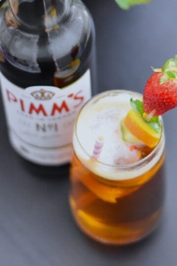 Pimms half and half with fruit skewers with a Pimms bottle next to the glass