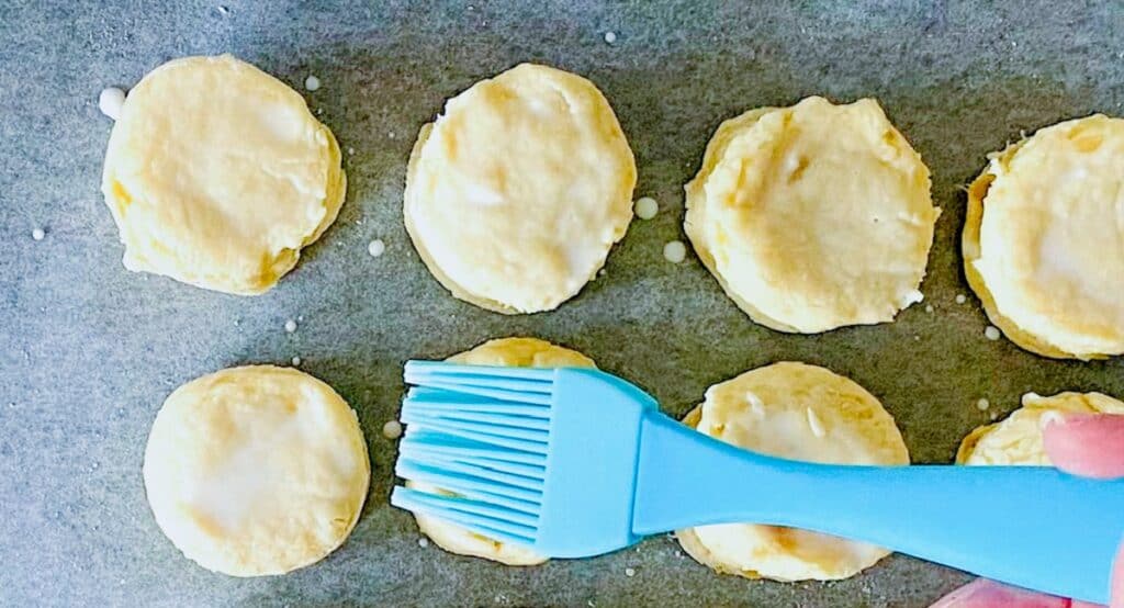 scones on a baking tray being brushed with milk on a pastry brush
