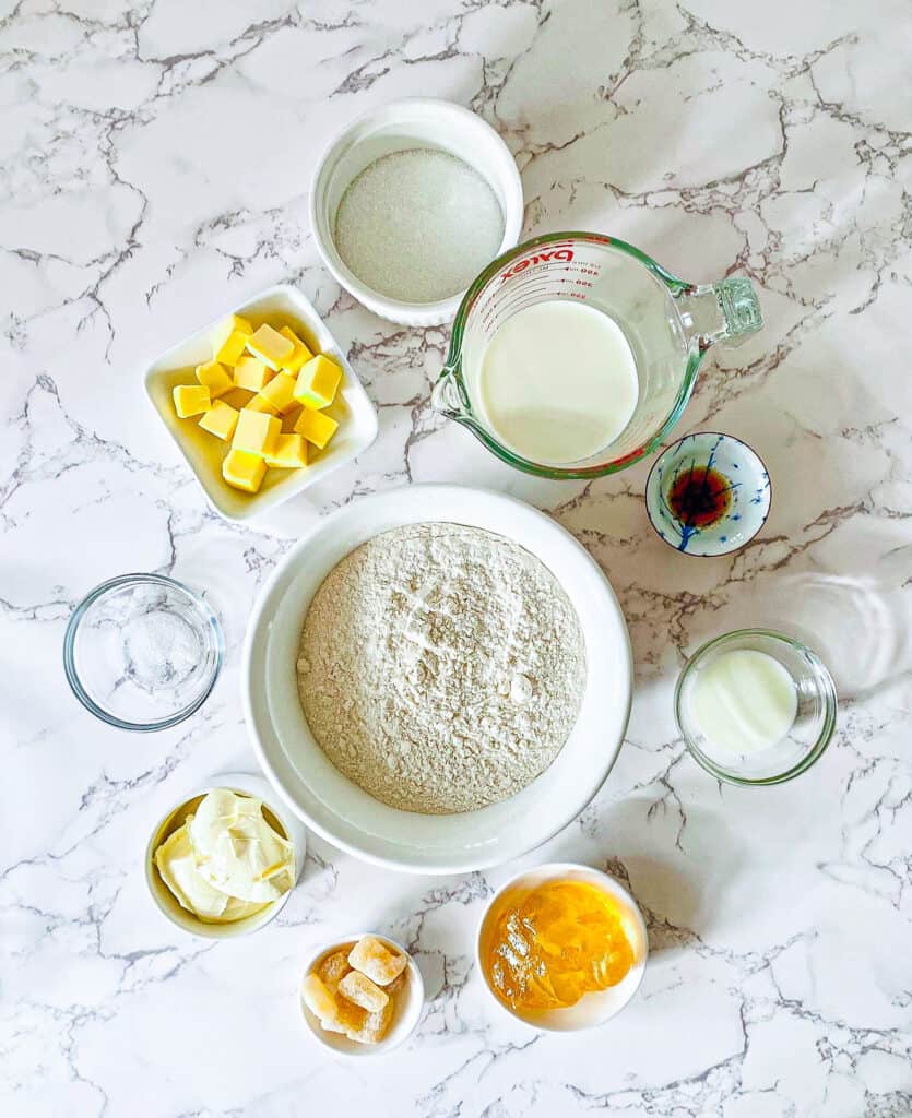 flour, butter, milk, crystallized ginger plus other ingredients sit on a marble bench. Laid out for Ginger scones recipe