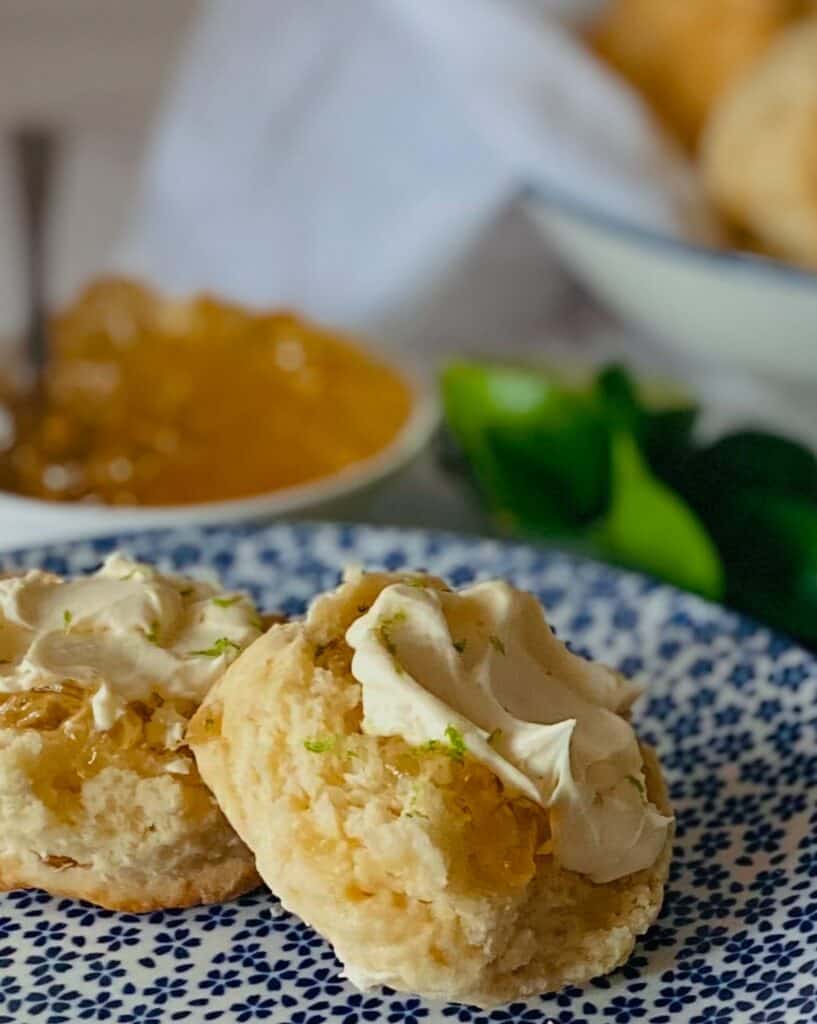 Two scones with marmalade and cream sit on a blue and white plate. Ginger scones recipe
