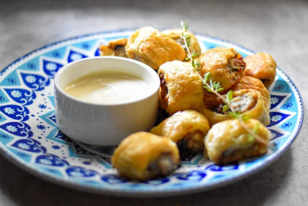 A plate with sausage rolls and a small bowl with dipping sauce