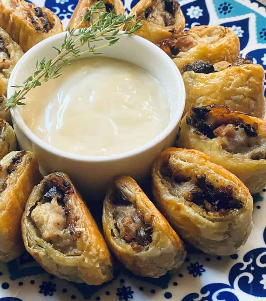 A plate of delicious Chicken Wellington Sausage Rolls with Honey Dijon Sauce garnished with a sprig of fresh thyme