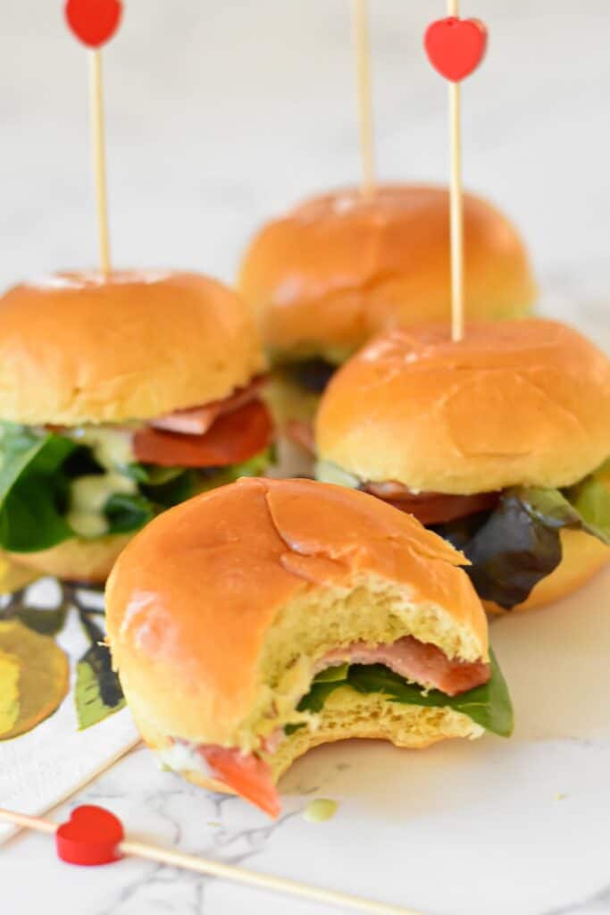 BLT sliders with green goddess dressing on a plate with love heart toothpicks. 