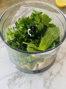 A food processor with a mix of fresh herbs