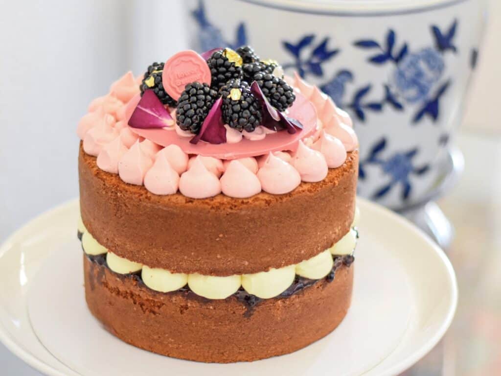 A Lemon and blackberry sandwich cake sits on a cake stand
