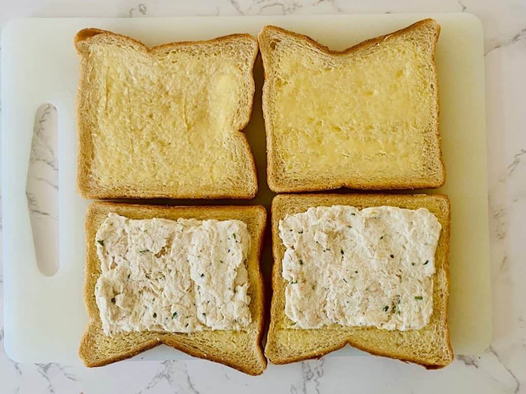 Four slices of bread spread with butter and chicken finger sandwich mixture