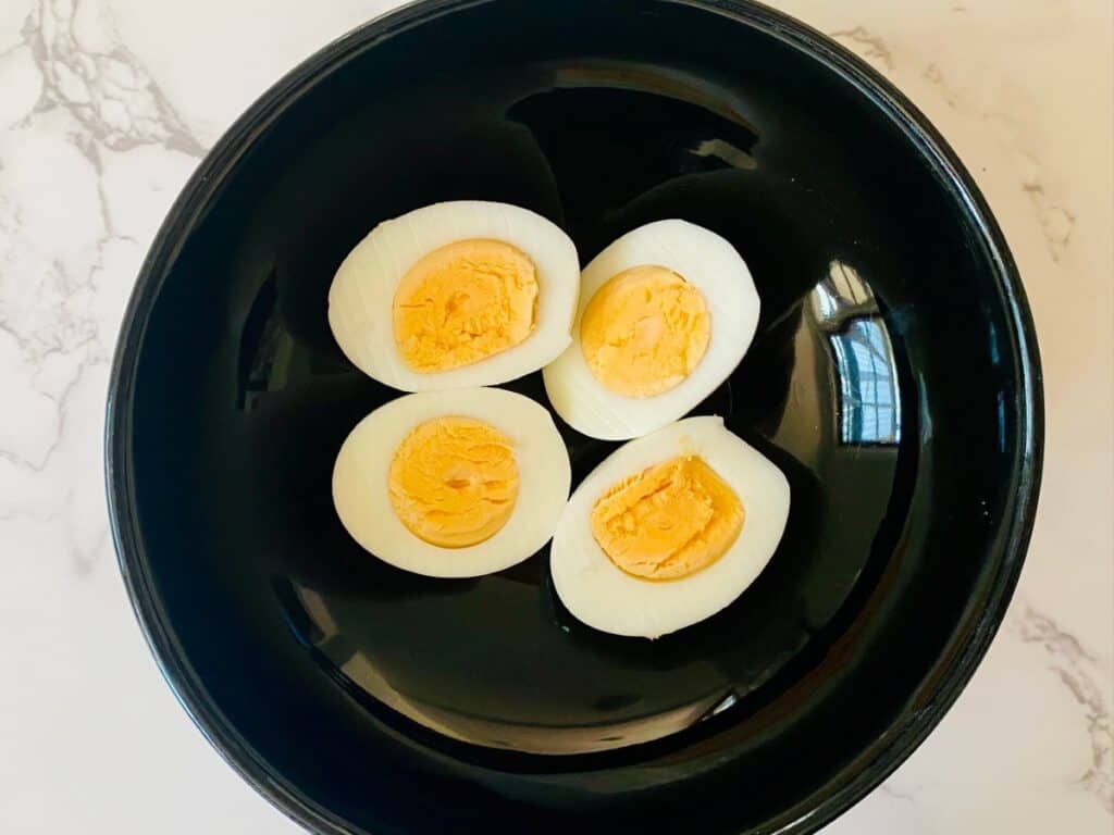 Two hard boiled eggs cut in half sit in a black bowl