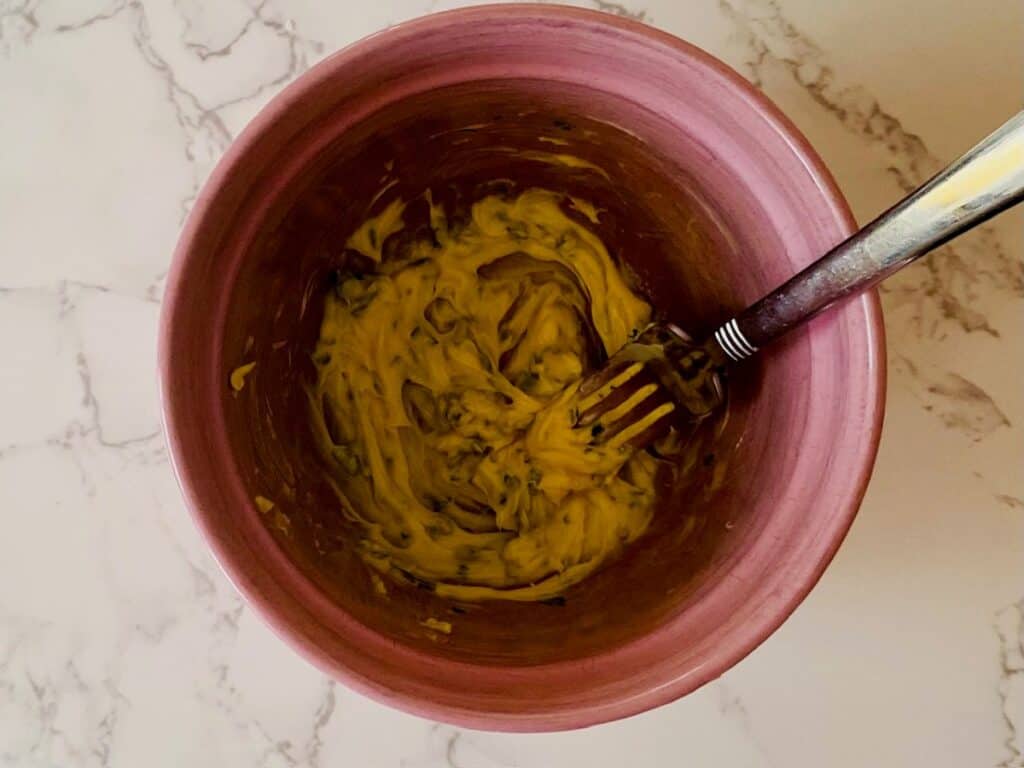 A pink bowl with a fork and softened butter flecked with parsley