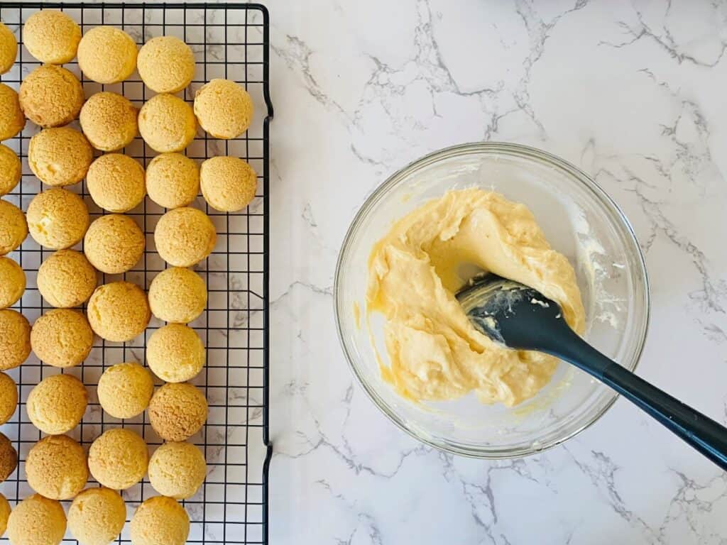 Vanilla Daisy Choux Puffs sit on a wire rack next to vanilla pastry cream