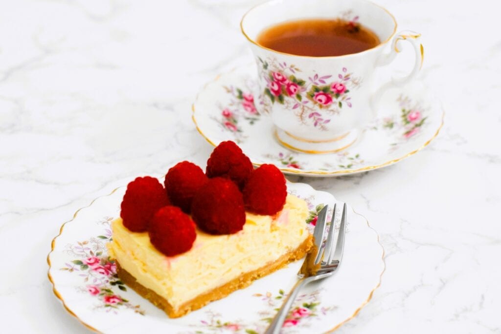 Raspberry White Chocolate Cheesecake slice on a plate with a tea cup and saucer