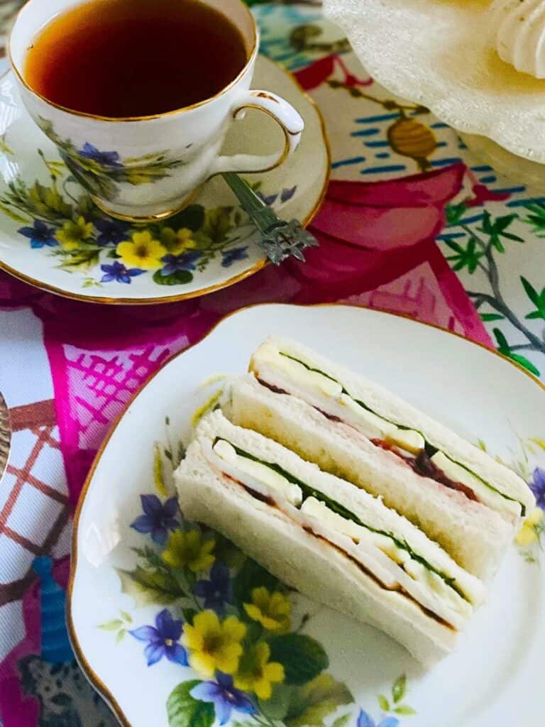 Turkey, cranberry & brie finger sandwiches on a plate with a teacup