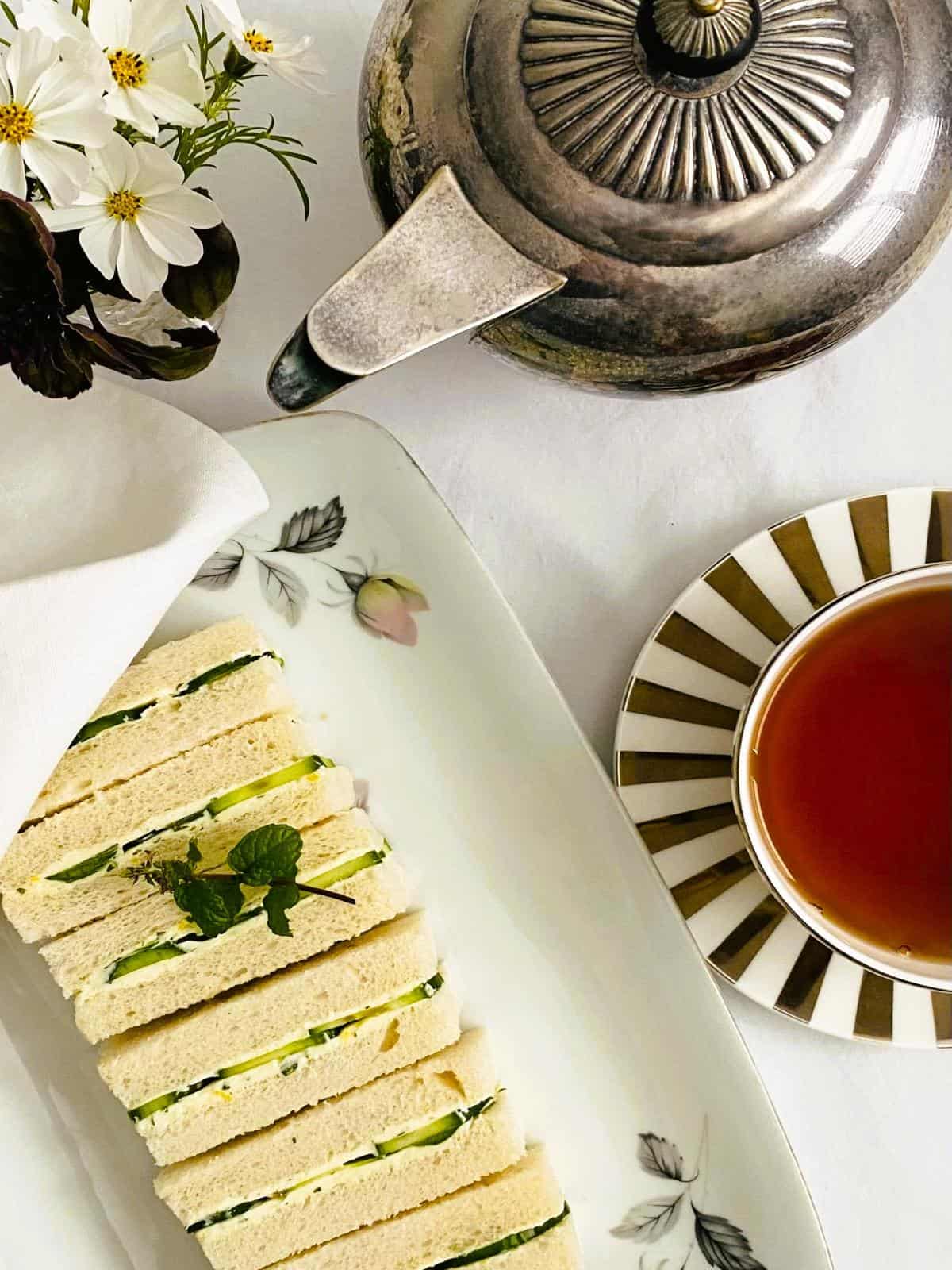 cucumber finger sandwiches on a tray with a silver teapot