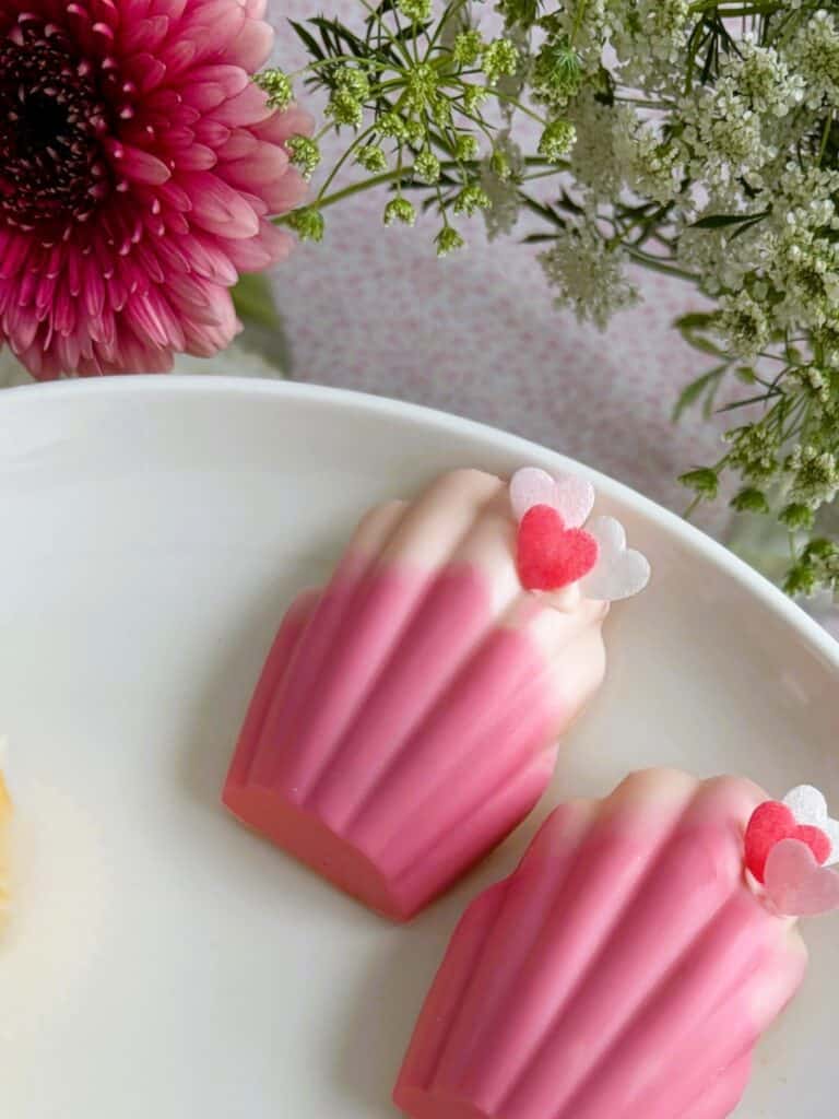 Easy ombre white chocolate madeleines with little hearts on a plate surrounded by flowers