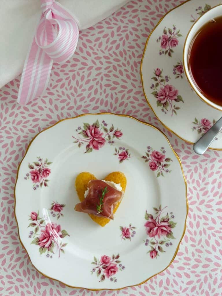 Prosciutto and goat's cheese heart on a plate with a cup of tea