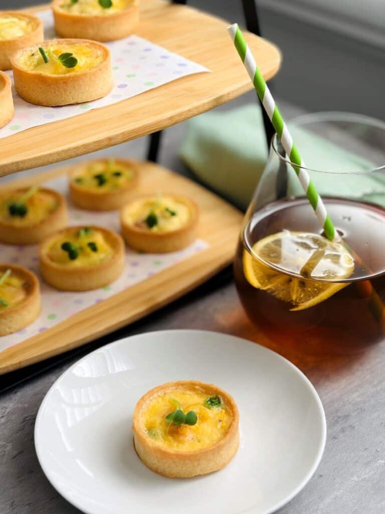 Salmon, Pea & Parmesan Tartlets on a tiered stand with a glass of iced tea with a green and white straw