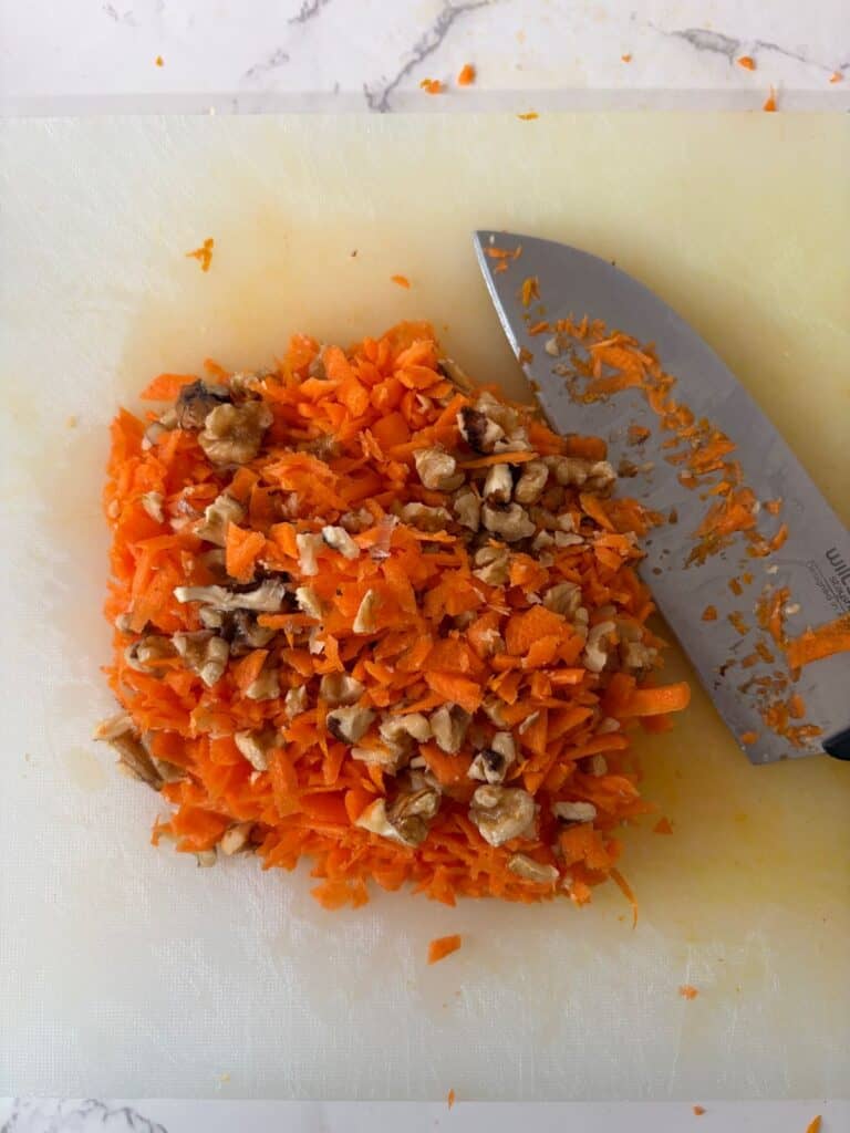 Walnuts, grated carrot and orange zest on a chopping board with a knife