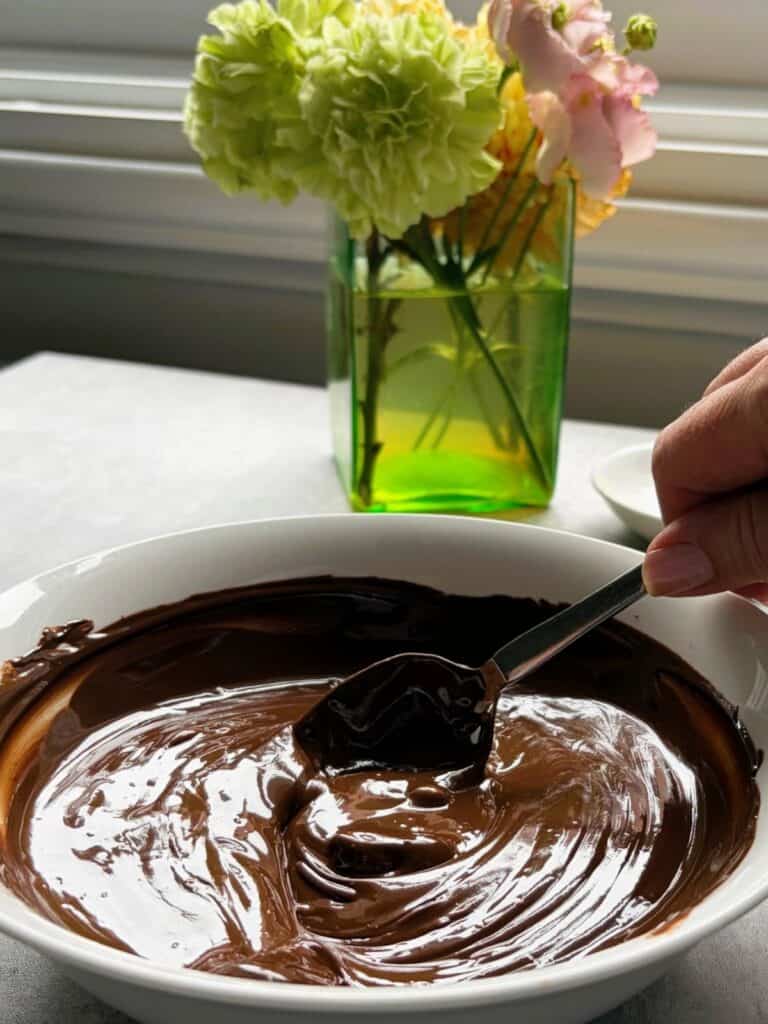 A vase of flowers and a bowl of melted chocolate with a spoon