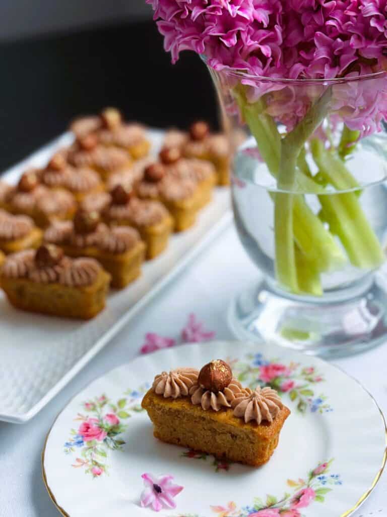 Hazelnut latte fingers on a single plate with a platter of fingers in the background and lilacs in a vase